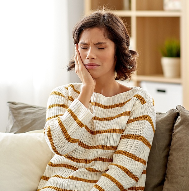 woman sitting on couch holding cheek in pain