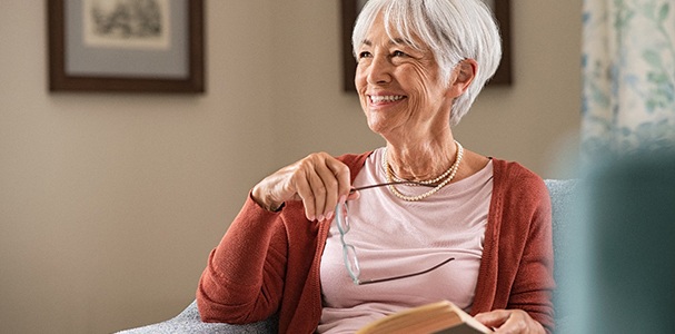 Woman smiling while holding book and glasses