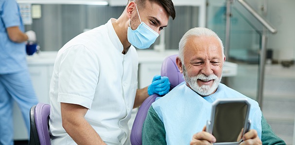Man smiling at reflection in small mirror with dentist