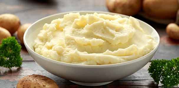 Bowl of mashed potatoes on table with potatoes and parsley