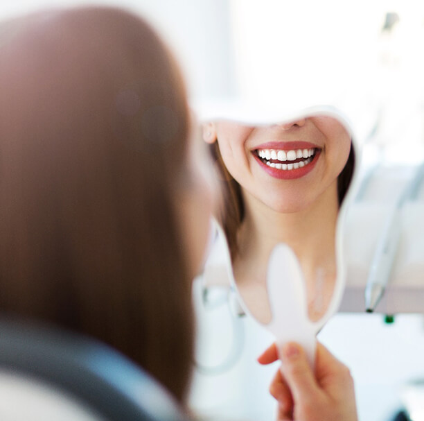 Woman with dental implants in Waupun and Beaver Dam smiling in mirror