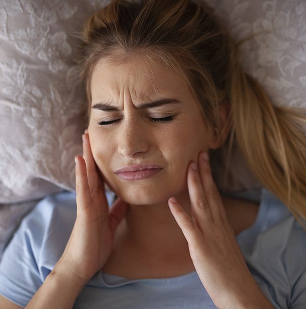 girl laying down holding jaw in pain