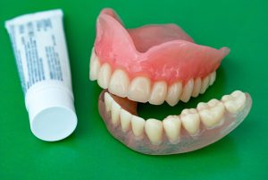 Set of dentures and bottle of adhesive on green background