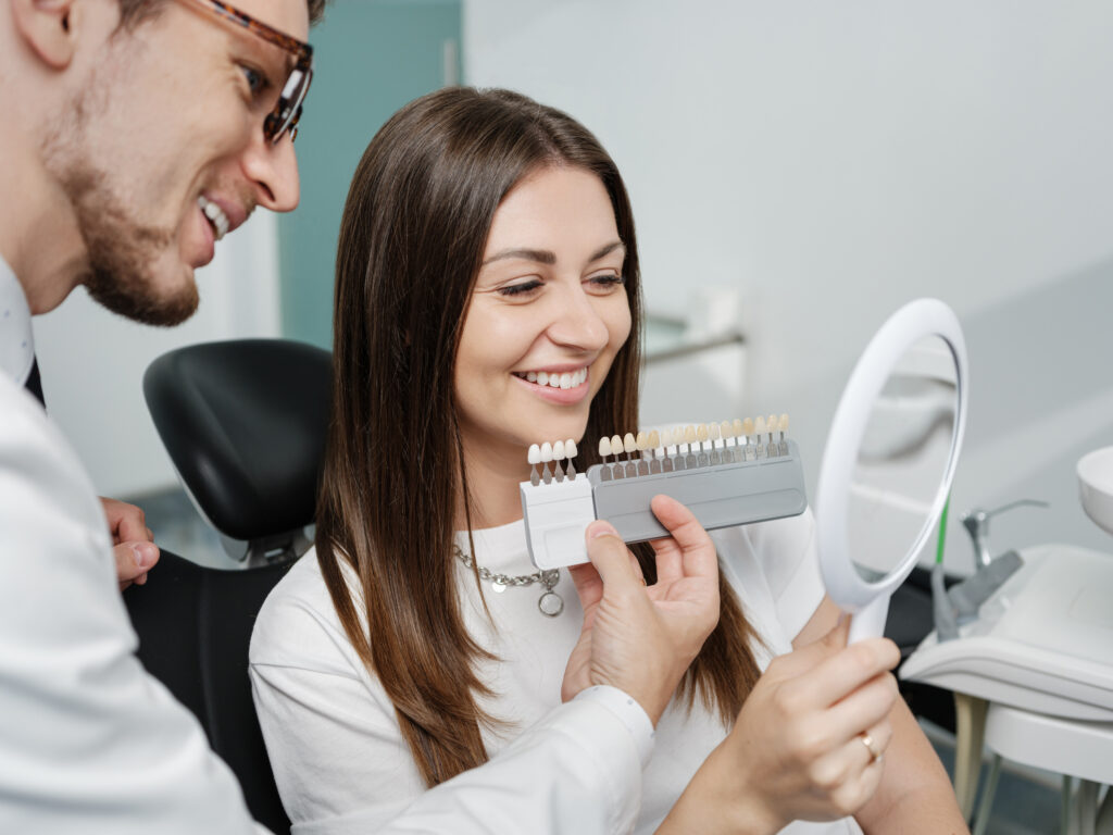 Woman smiling at mirror while dentist holds up veneers